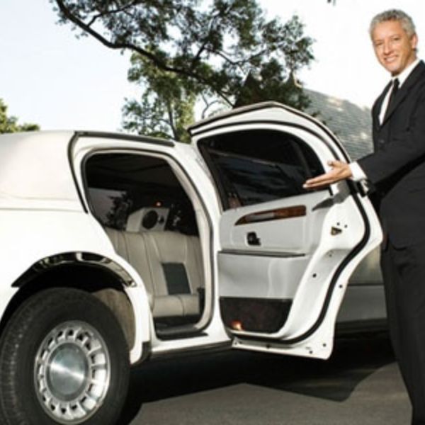 Professional chauffeur opening door of a white stretch limousine.