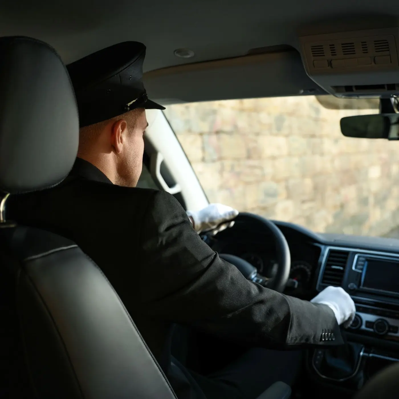 A professional chauffeur in a uniform and white gloves driving a luxury vehicle.