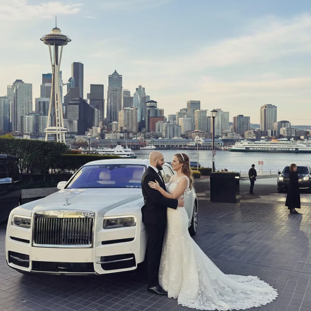 A bride and groom embracing in front of a white luxury Rolls Royce with the Seattle skyline and Space Needle in the background