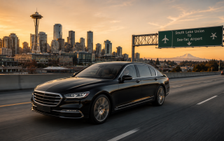 Luxury black sedan driving on a Seattle highway at sunset with skyline
